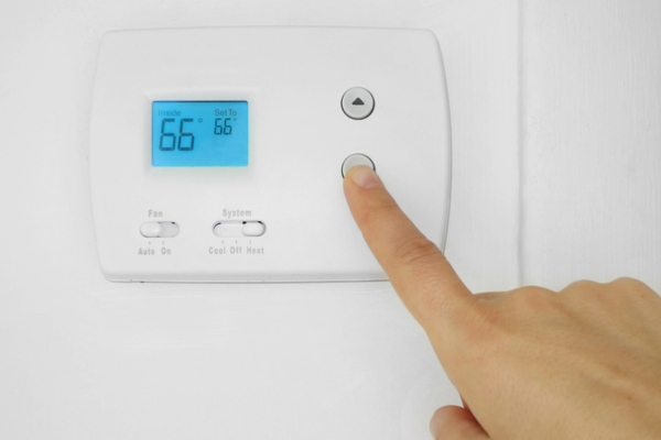 homeowner adjusting home thermostat to low level that can overburden the AC system