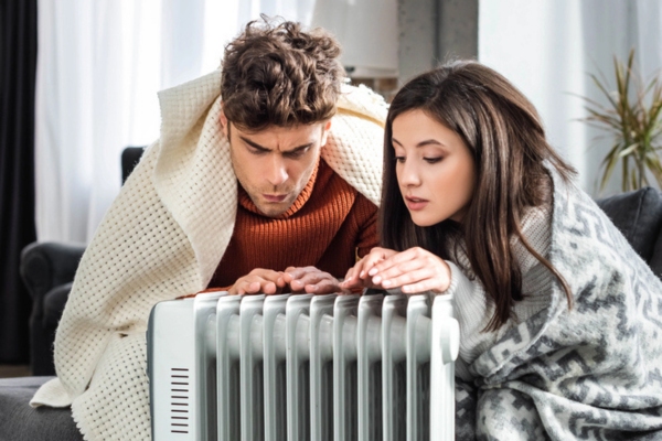 couple feeling cold sitting by a space heater due to cold indoor temperature depicting frozen heating oil symptoms