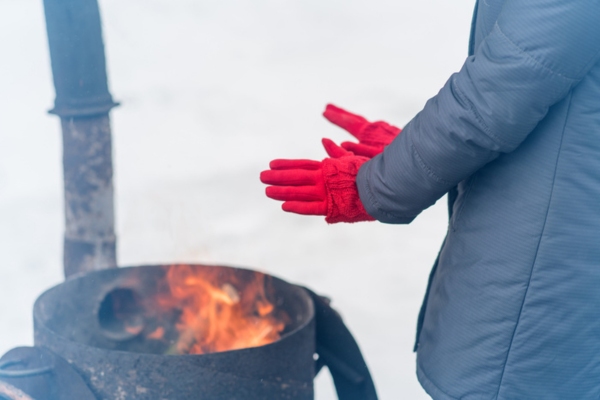 cropped view of a woman in red gloves keeping warm in an outdoor fire depicting history of heating