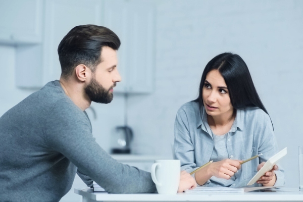 Woman holding calculator while talking to her husband depicting comparative review of will call vs automatic oil delivery